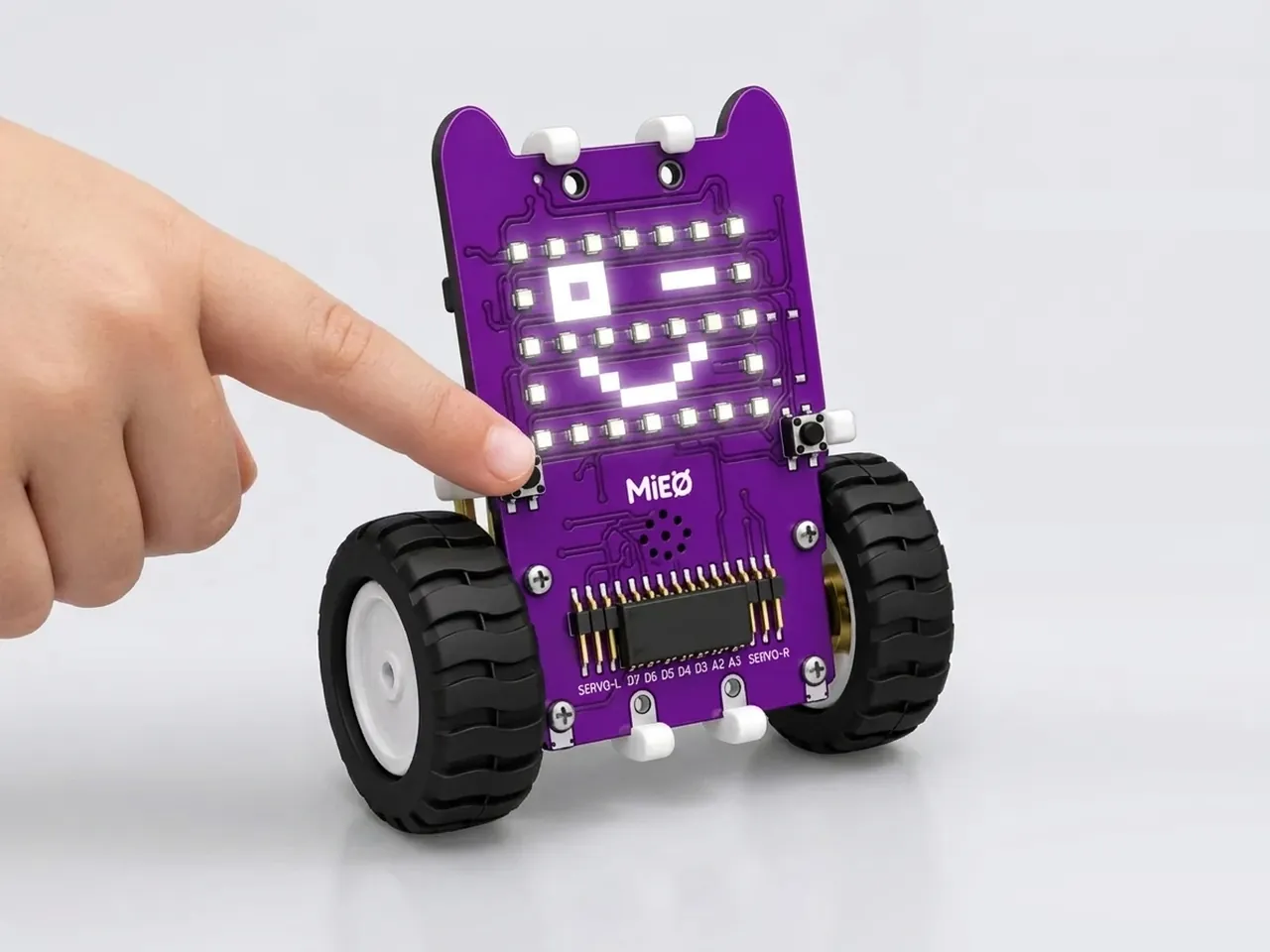 A finger presses MIEO's button while its LED matrix shows a winking face