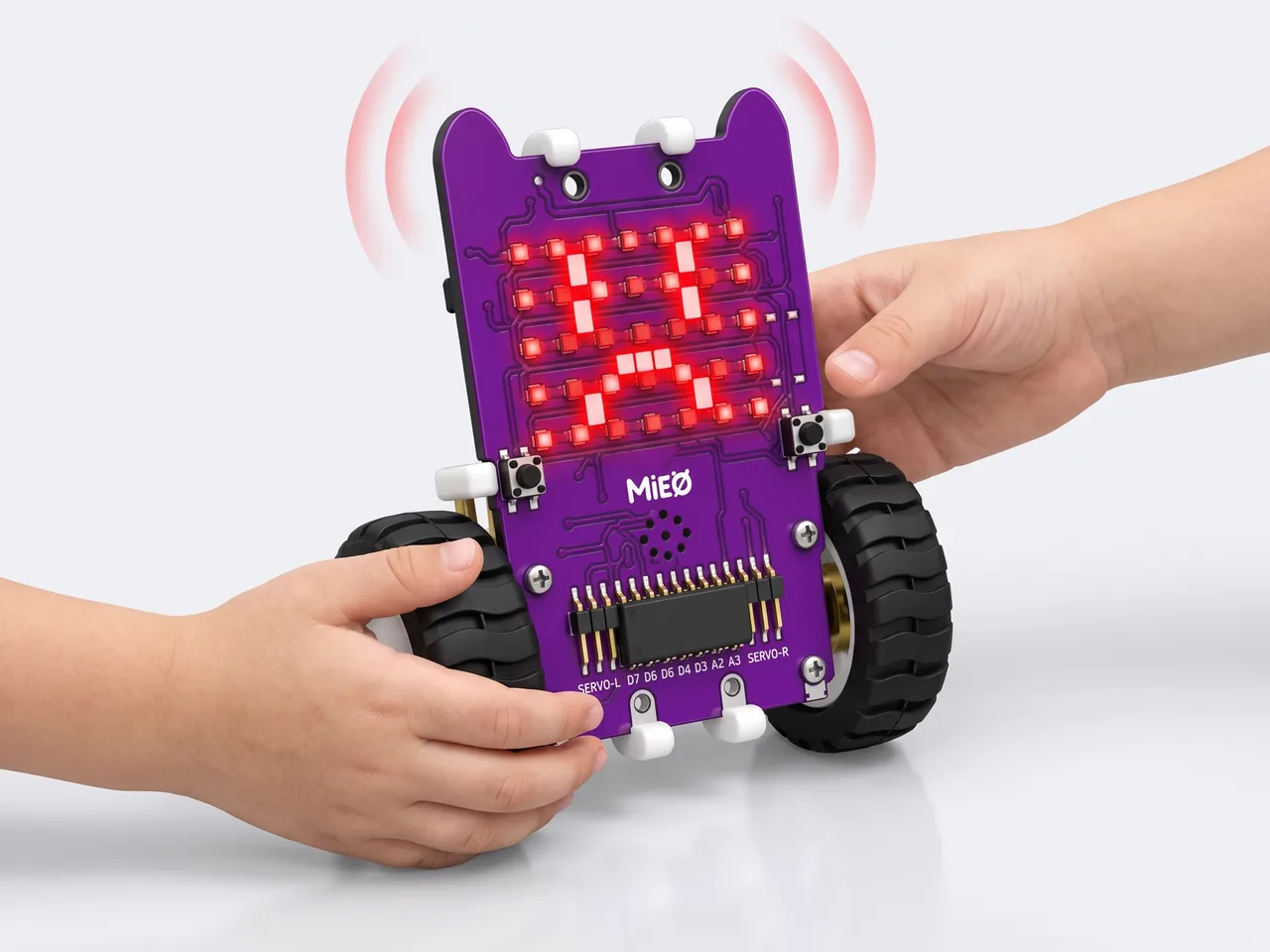 Two children's hands passing an upright MIEO whose LED grid shows an angry face as it sounds its alarm