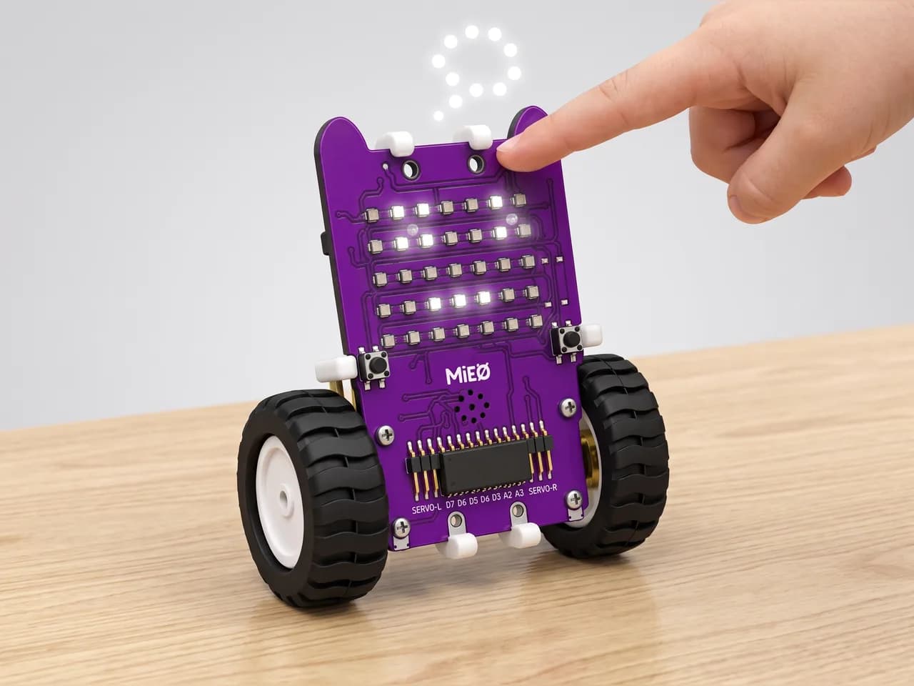 Upright MIEO with a thinking face on its LED grid as a child's fingertip presses its button